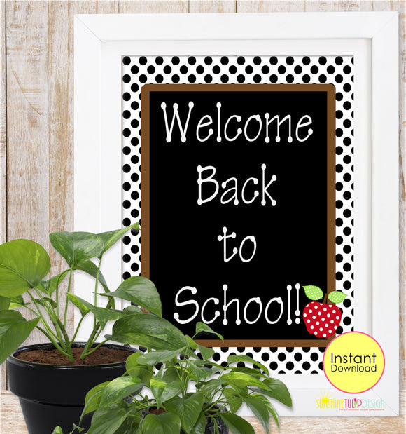 A framed 'Welcome Back to School' sign with a black center, white polka dot border, and a red apple illustration, displayed on a desk with books, an apple, and pencils.